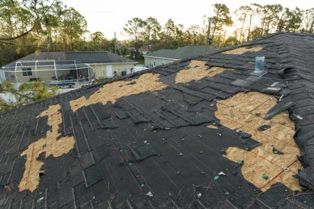 Ruined rooftop in need of repair. Wind damaged house roof with missing asphalt shingles after hurricane Ian in Florida.