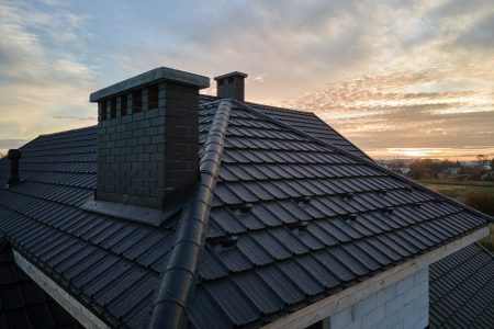 Snow guard for safety in winter on house roof top covered with ceramic shingles. Tiled covering of building.